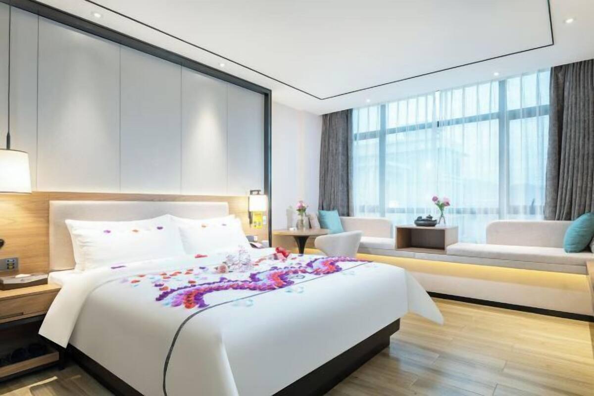 A modern hotel room with a large bed, a sofa, a nightstand, and a window with curtains.