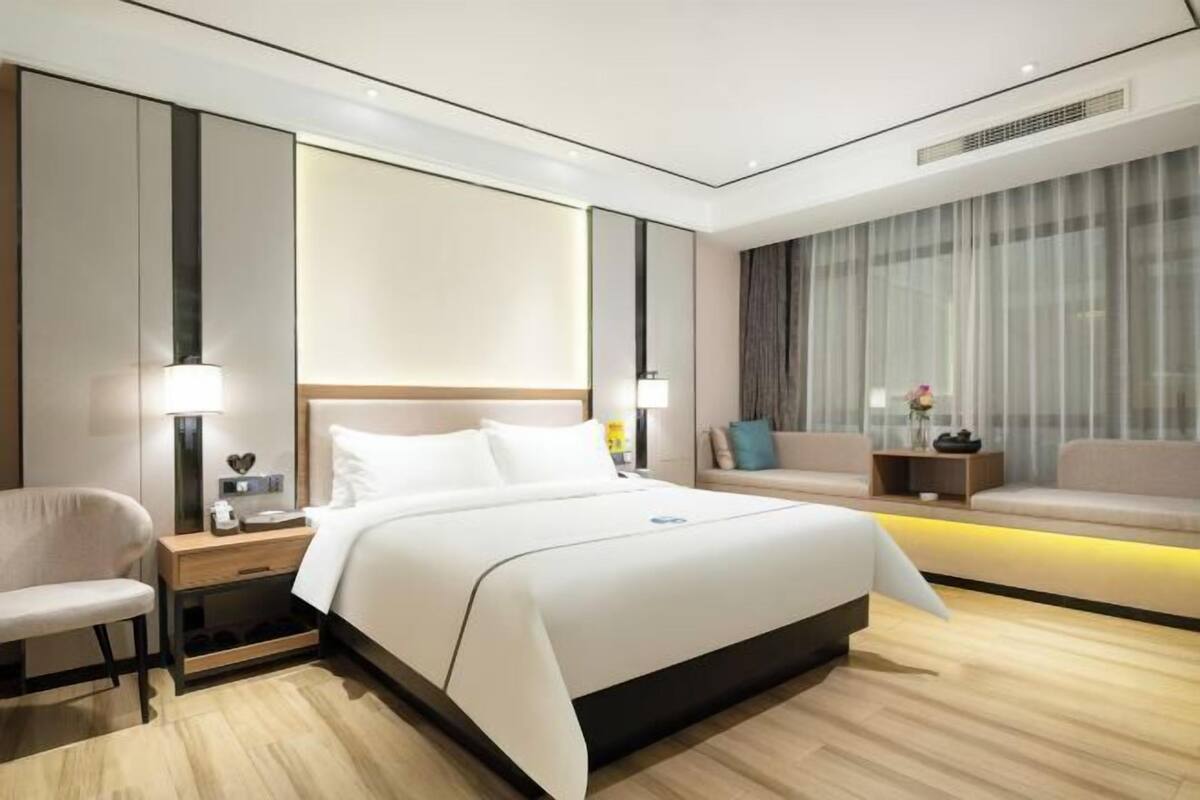 A modern hotel room with a large bed, bedside tables, a chair, and a sofa.
