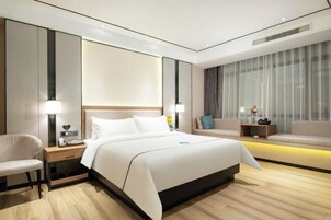 Una habitación de hotel moderna con una cama grande, mesitas de noche, una silla y un sofá.