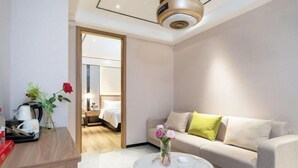 Een moderne hotelkamer met een ronde salontafel, een bank met kussens, een houten bijzettafeltje met een bloevas en een bed op de achtergrond.