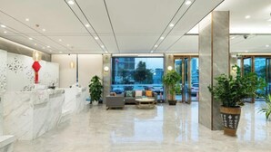 Een moderne hotel lobby met een marmeren receptiebalie, een zithoek en grote ramen met uitzicht op de stad.