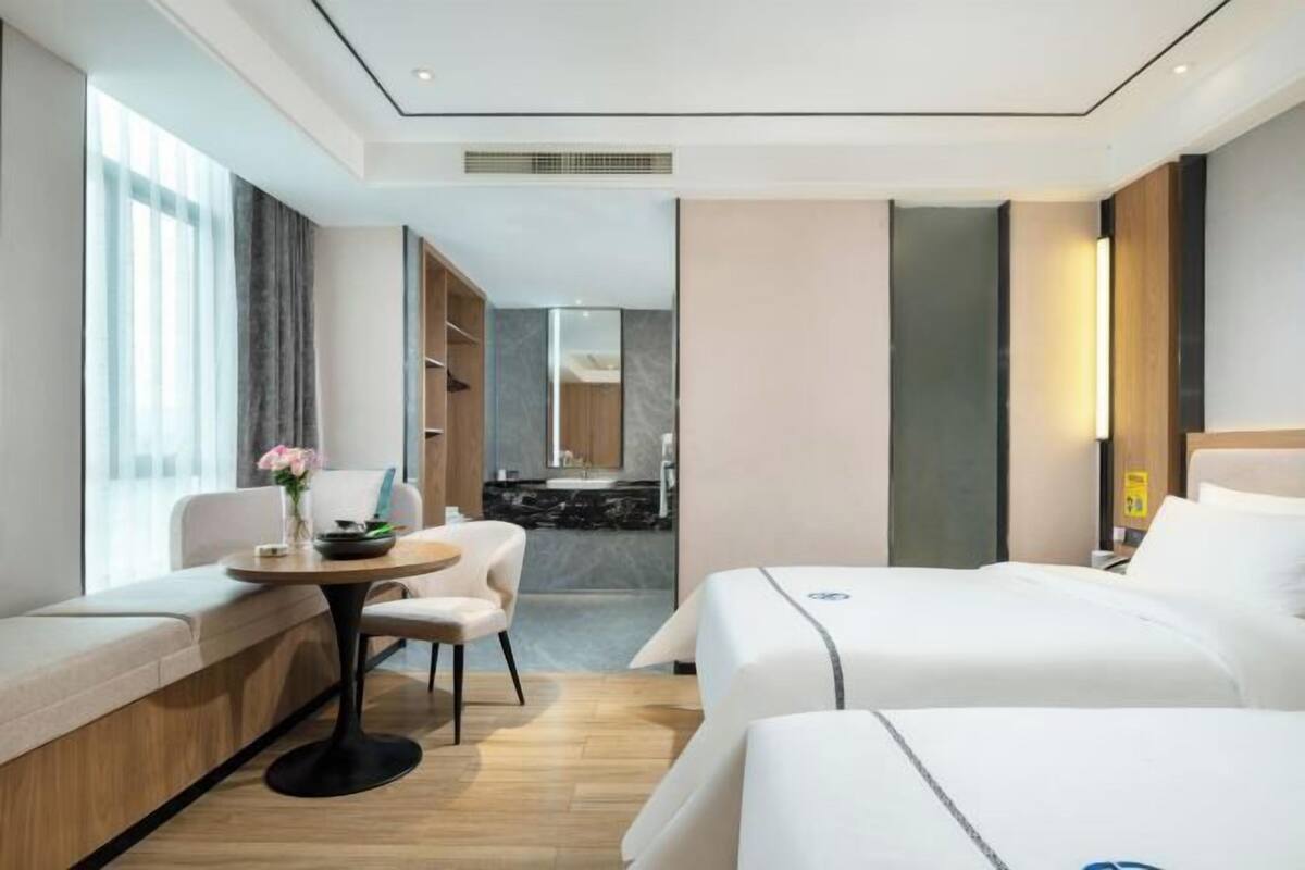 A hotel room with two beds, a seating area, a small table, and a view of the bathroom.