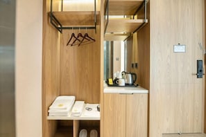A compact hotel room with a wooden interior, a small kitchenette, and a hanging clothes rack.