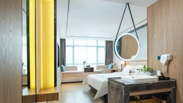 Een moderne hotelkamer met een bed, nachtkastje en een badkamer met een marmeren wastafel en spiegel.