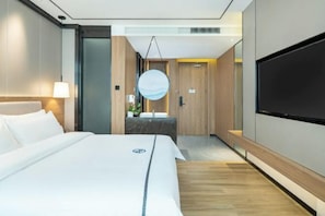 A modern hotel room with a large bed, a flat-screen TV, a round mirror, and a small bathroom area.