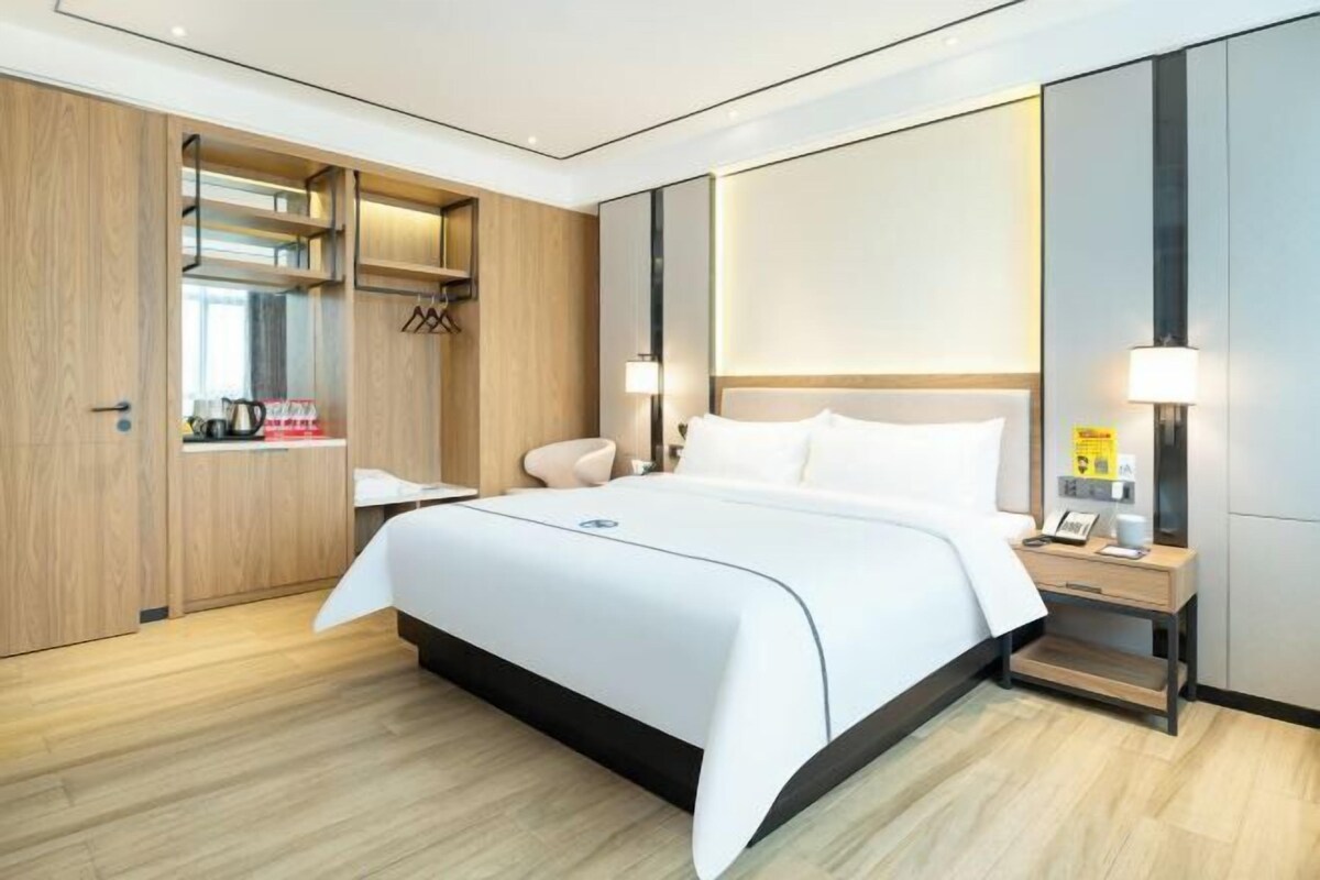 A modern hotel room with a large bed, bedside tables, a wardrobe, and a mirror.