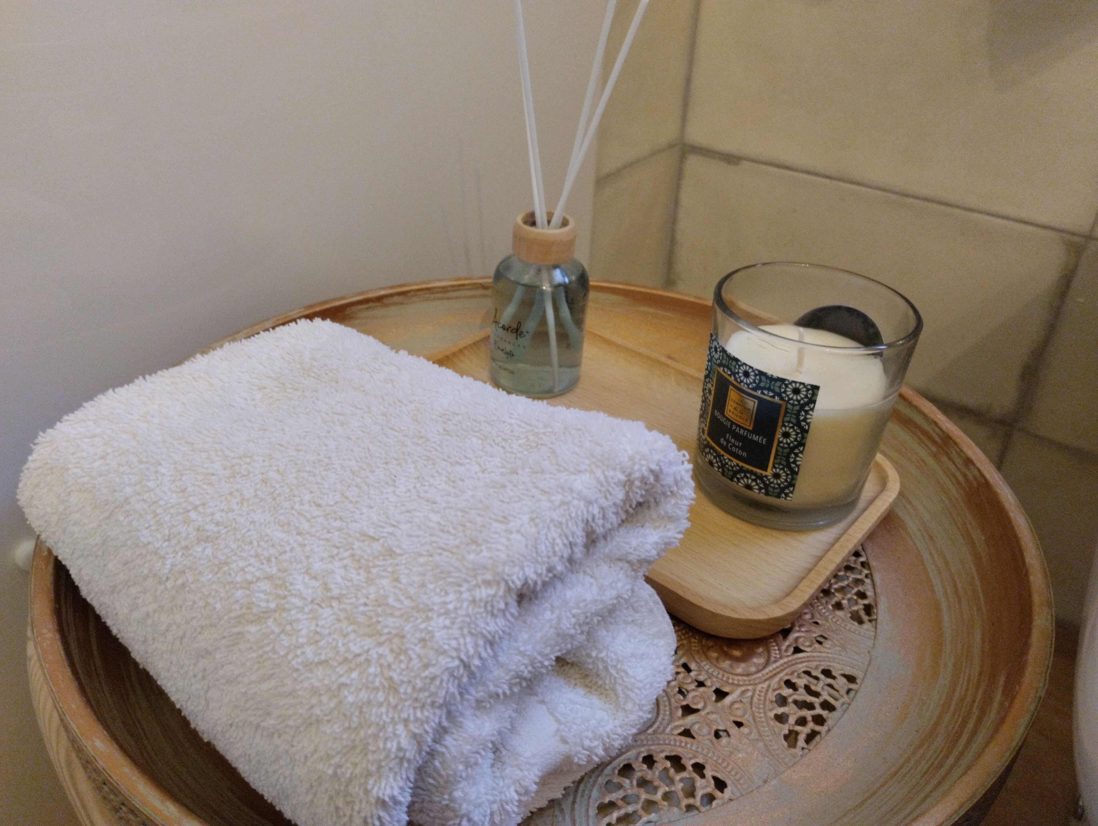 A white towel on a tray with a candle and a bottle of reed diffuser.