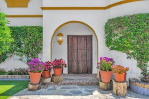 Une cour avec une porte en bois, des plantes en pot et un sol carrelé.