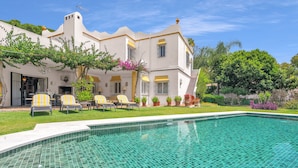 A poolside view of a house with a tiled pool, outdoor seating, and lush greenery. - Villa Arin - Beachside Family Home (Estepona)