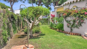 A well-maintained garden with a pathway, a tree, and a white building with a tiled roof. - Villa Arin - Beachside Family Home (Estepona)