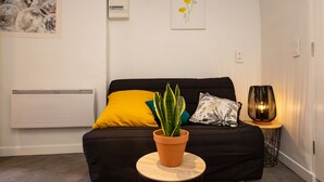 Ein modernes Wohnzimmer mit einer schwarzen Couch, einem runden Holztisch mit einer Topfpflanze und einer dekorativen Lampe.