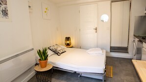 Ein ordentlich eingerichtetes Schlafzimmer mit einem Bett, Nachttisch, Lampe und einem Topf mit Pflanze.