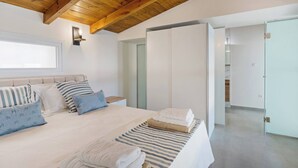 Een moderne slaapkamer met een houten plafond, een groot bed met gestreept beddengoed en uitzicht op een badkamer door een open deur.
