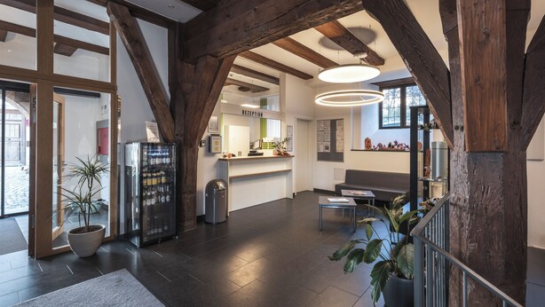 Un vaste espace d’accueil au design moderne, agrémenté de poutres apparentes, d’un comptoir de réception et d’un coin salon.