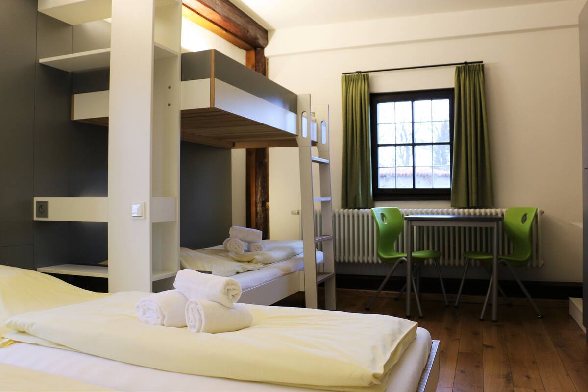 Une chambre avec un lit superposé, un bureau et des chaises, un radiateur et une fenêtre avec des rideaux.
