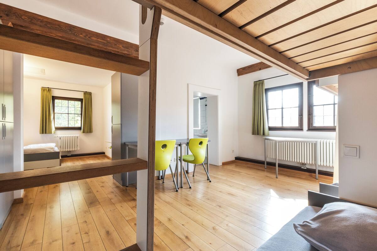 Un intérieur moderne avec des planchers en bois, un coin repas avec des chaises jaunes et de grandes fenêtres qui laissent entrer la lumière naturelle.