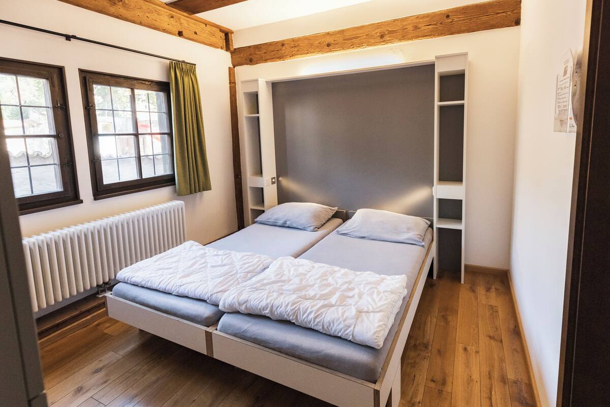 Une chambre à coucher avec un lit, une fenêtre, un radiateur et des poutres en bois au plafond.