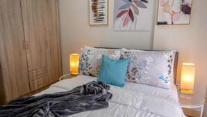 A bedroom with a bed, a blanket, two wall-mounted lamps, a wardrobe, and two framed artworks. - Delightful Apartment Holiday Rental (Davao City)