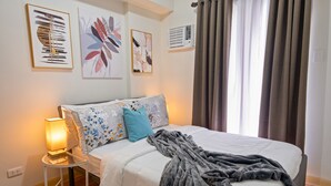 A neatly made bed with a white comforter and decorative pillows, a bedside lamp, and a gray throw blanket. - Delightful Apartment Holiday Rental (Davao City)