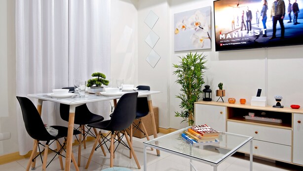 A modern dining area with a glass table, black chairs, and a white tablecloth. - Delightful Apartment Holiday Rental (Davao City)