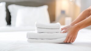 Un montón de toallas blancas ordenadas sobre una cama, con un almohadón blanco al fondo.