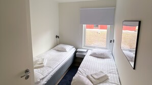 Una habitación pequeña y moderna con dos camas individuales, una mesita, un ventanal con vistas y un detector de humo en el techo.