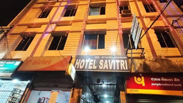 Un bâtiment avec une enseigne indiquant « HÔTEL SAVITRI » et un distributeur automatique de billets de la « Punjab National Bank ».