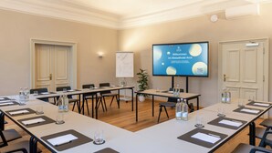 Une salle de conférence équipée d’une longue table, de chaises, d’un tableau blanc et d’un écran affichant du texte.