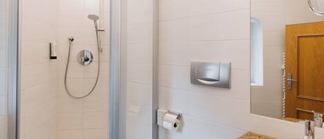 Un baño moderno con ducha de vidrio, lavamanos blanco y puerta de madera.