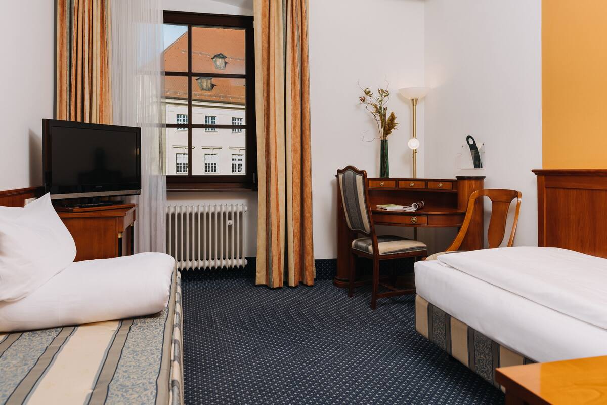 A hotel room with a bed, a desk, a chair, a TV, and a window with curtains.