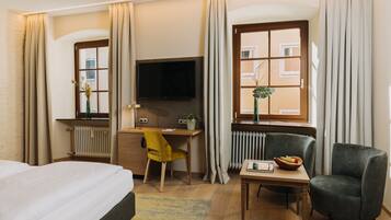 Ein Hotelzimmer mit einem Bett, einem Schreibtisch mit Computer, einem Fernseher, einem Sessel und einem kleinen Tisch mit Obstschale.