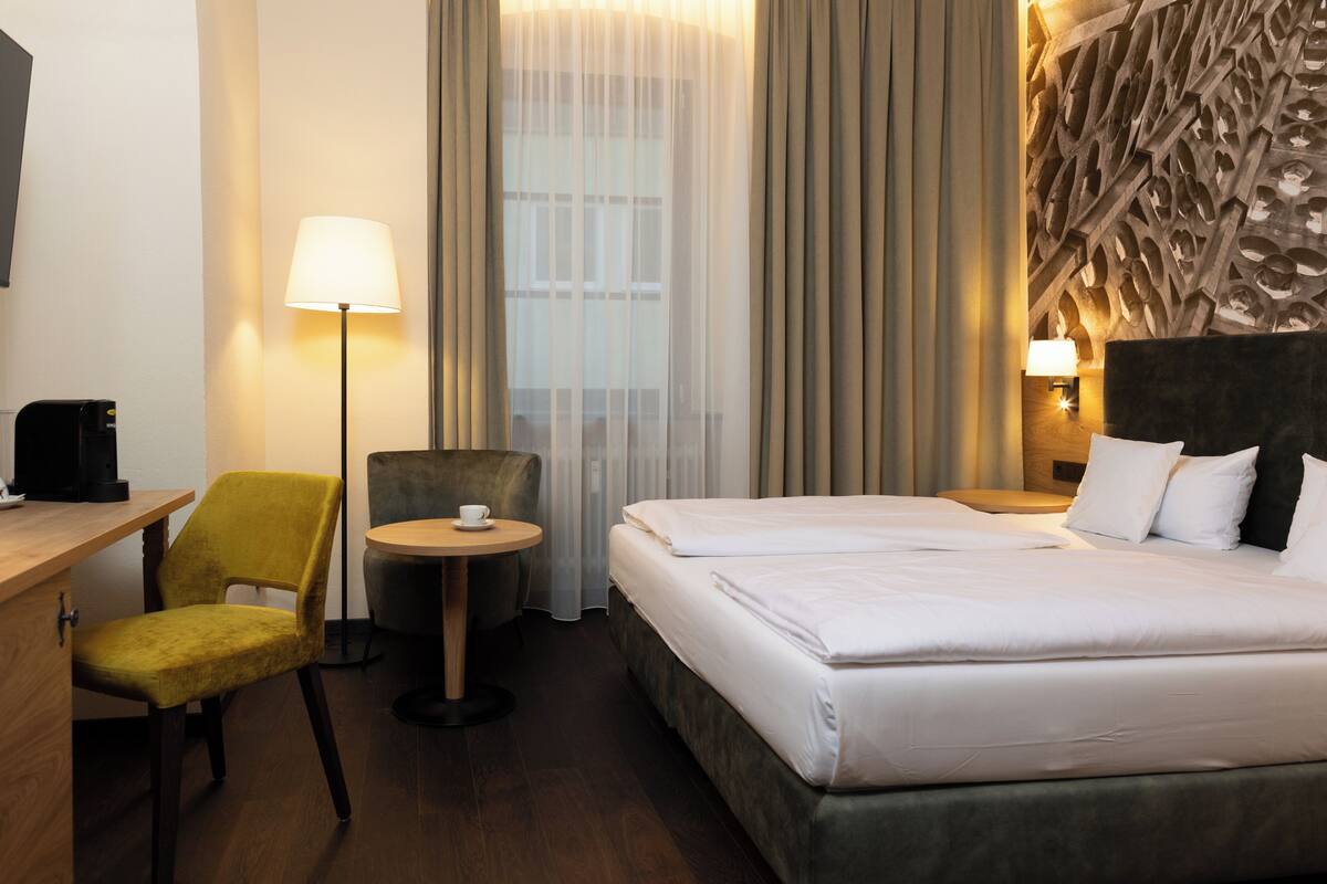 A hotel room with a bed, a desk, a chair, a lamp, and a wall with a unique design.