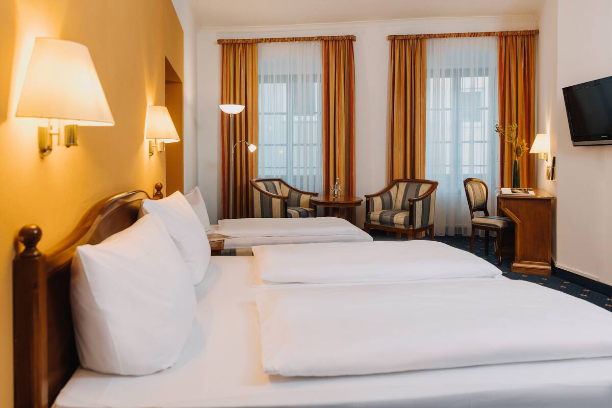 A hotel room with two beds, a desk with a chair, a television, and lamps.