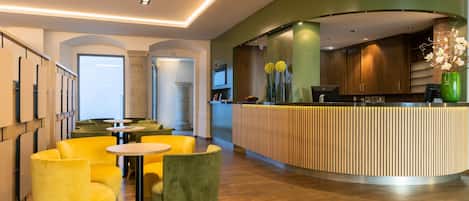 Una zona de recepción moderna con un mostrador curvo de madera, sillas tapizadas en amarillo y verde, y una pared de acento verde.
