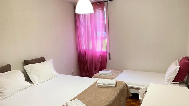 A hotel room with two beds, a small table, and a hanging light fixture. - Duplex proximo do aeroporto lisboa (Lisboa)
