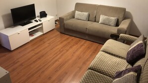 A living room with a flat-screen TV, a white entertainment unit, a beige sofa, and a patterned armchair. - Duplex proximo do aeroporto lisboa (Lisboa)