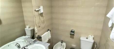 Une petite salle de bain compacte, équipée de deux lavabos, d’un bidet, de toilettes et d’une poubelle.