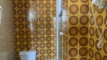 Un baño con baldosas amarillas y marrones con diseño, un inodoro blanco, una zona de ducha y una toalla colgada en la pared.