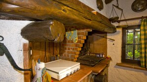 A rustic kitchen with a wood-burning stove, brick walls, and a window with a checkered curtain. - Moon Nest - Apartment in villa, 10 min from the sea private garden pool (Massarosa)