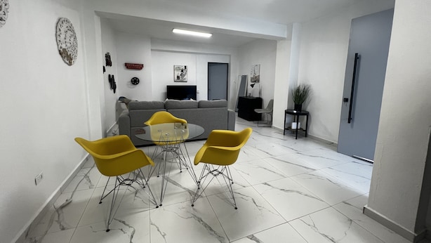A modern living room with a grey sofa, yellow chairs, and a glass coffee table. - Spacious place (San Juan)