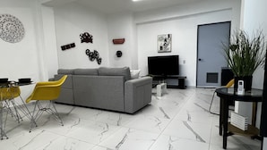 A modern living room with a grey sofa, yellow chairs, a flat-screen TV, and a dining area with a small table and chairs. - Spacious place (San Juan)