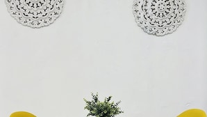 A dining area with a round glass table, four yellow chairs, a potted plant, and two decorative wall pieces. - Spacious place (San Juan)