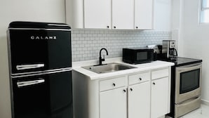 A compact kitchen with white cabinets, a black refrigerator, a microwave, and a stove. - Spacious place (San Juan)