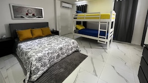 A bedroom with a bed, a bunk bed, a nightstand, a lamp, a painting, and an air conditioning unit. - Spacious place (San Juan)