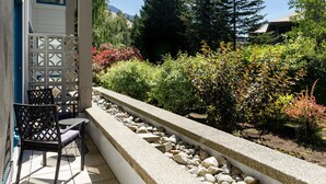 A patio with a seating area, a stone planter with rocks, and a variety of shrubs and trees in the background.