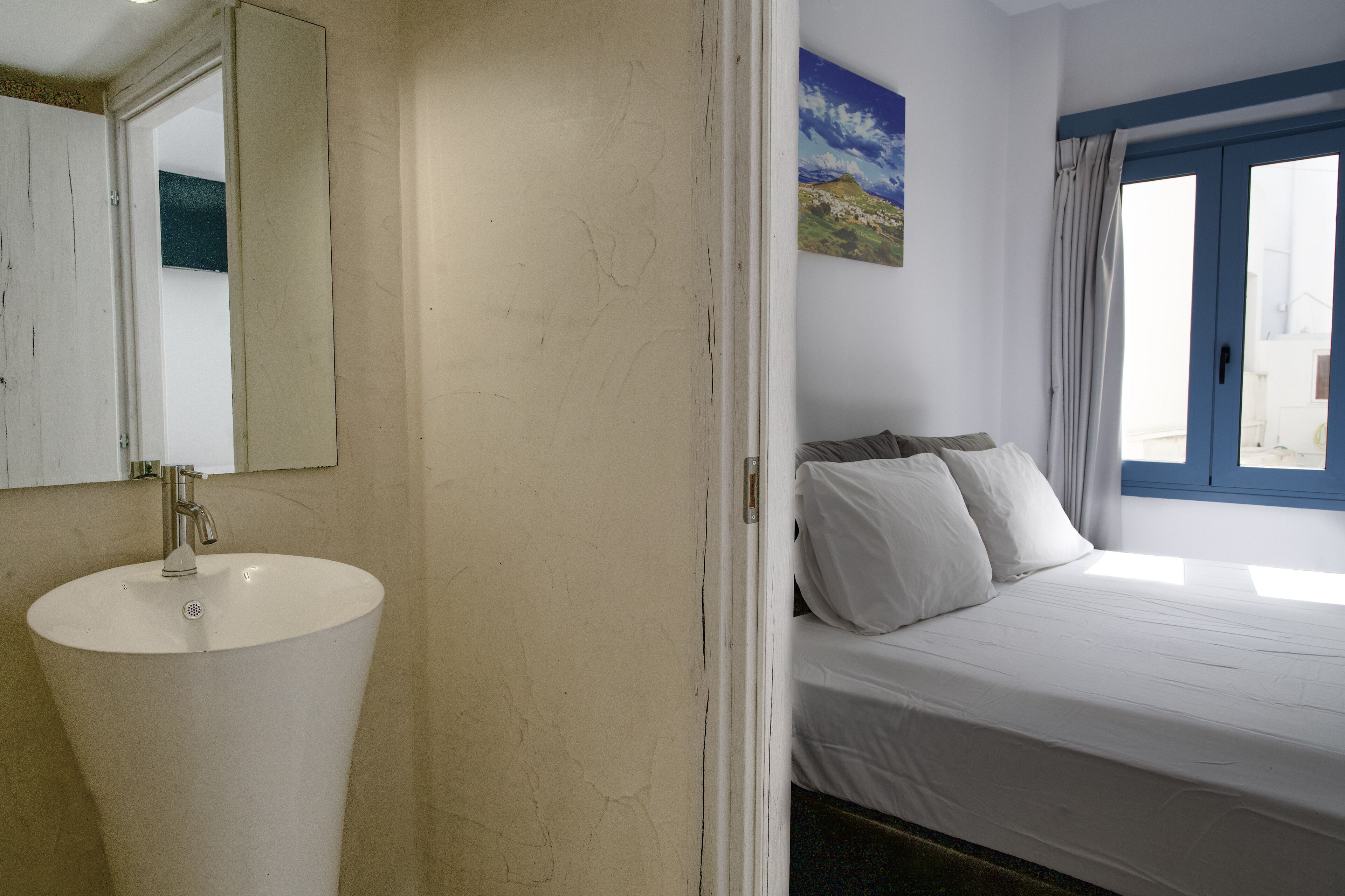 Un baño con un lavamanos blanco y una cama con ropa de cama blanca.