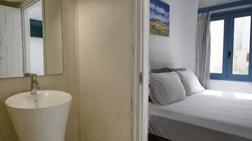 Un baño con un lavamanos blanco y una cama con ropa de cama blanca.