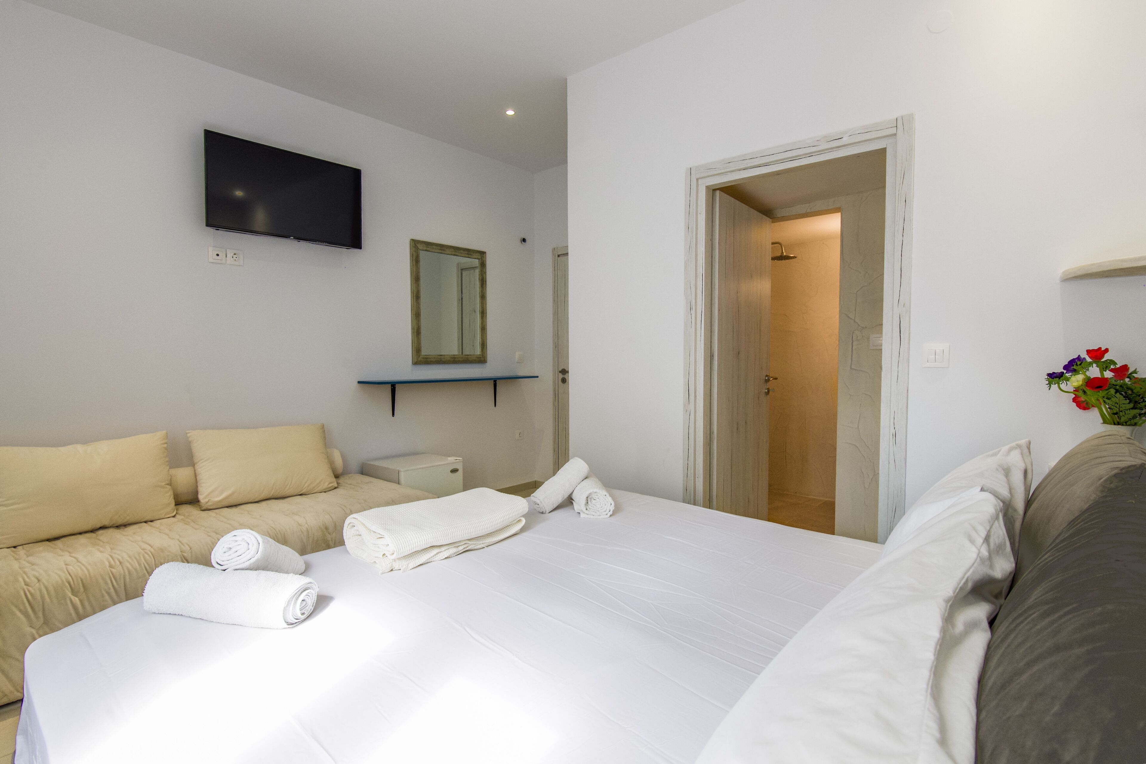 Una habitación de hotel con cama, sofá, televisión, espejo y puerta que da a un baño.