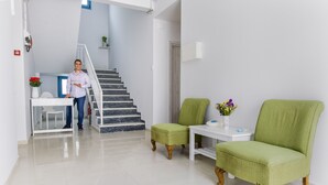 A modern living room with a staircase, a green armchair, a white table, and a vase with flowers. - Porto Bello Hotel (Paros)