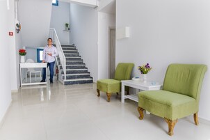 A modern living room with a staircase, a green armchair, a white table, and a vase with flowers.